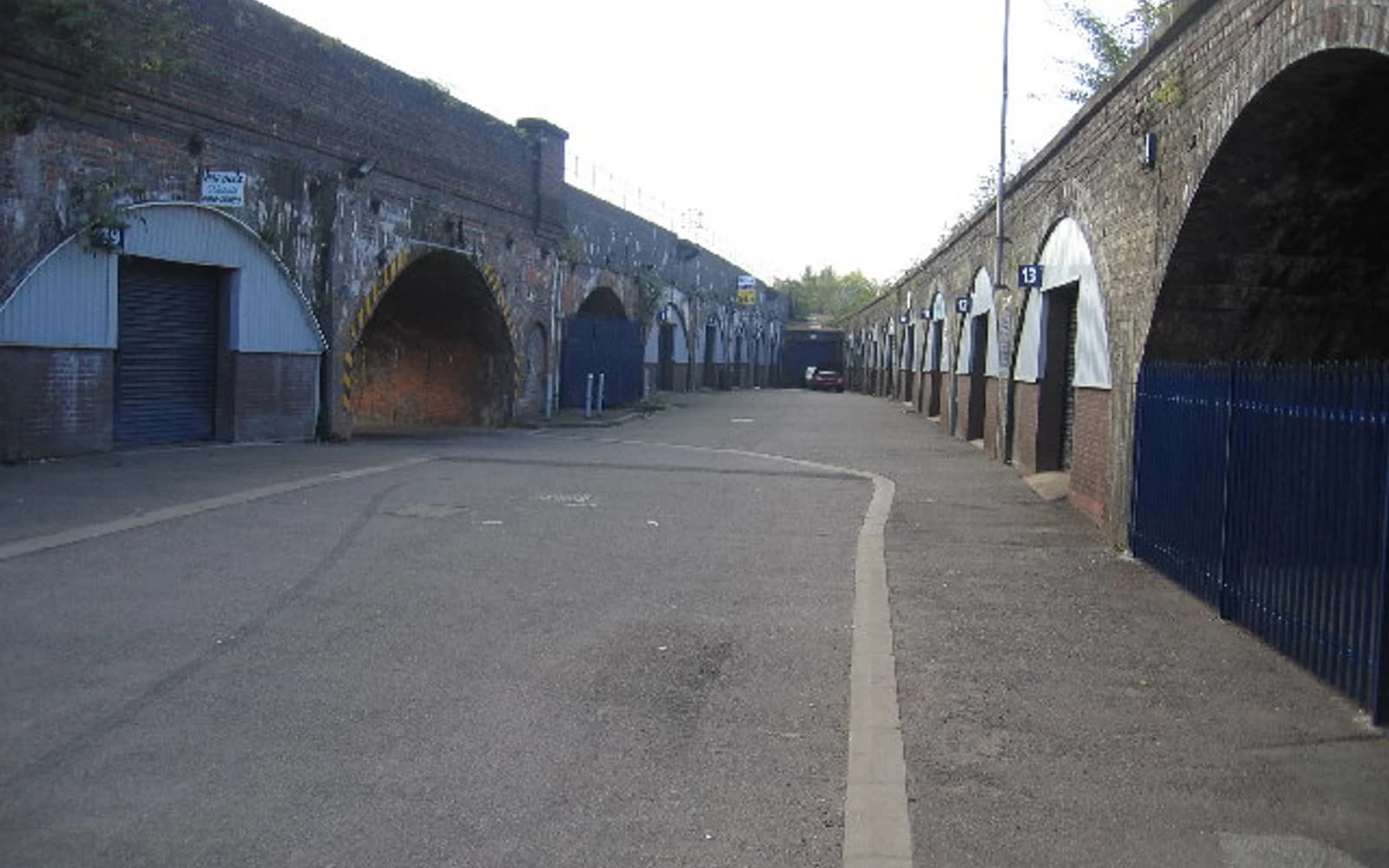 A quiet service road lined with brick railway arches and small industrial units in Leamington Spa.