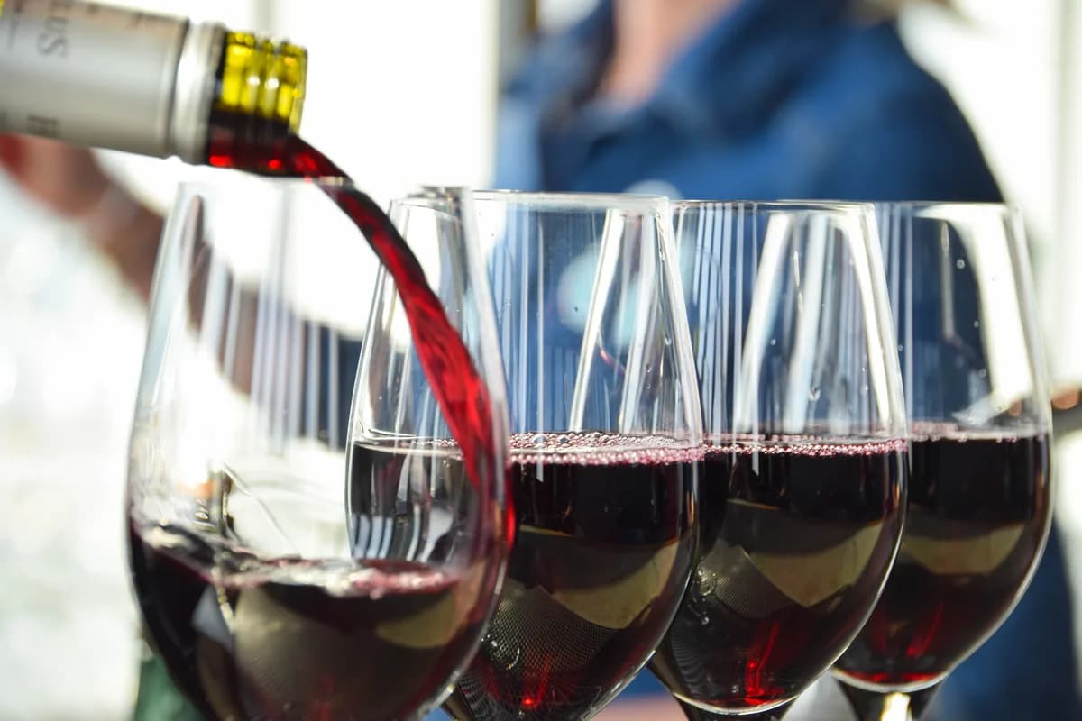 Red wine being poured into four clear glasses, with an indistinct person in the background.